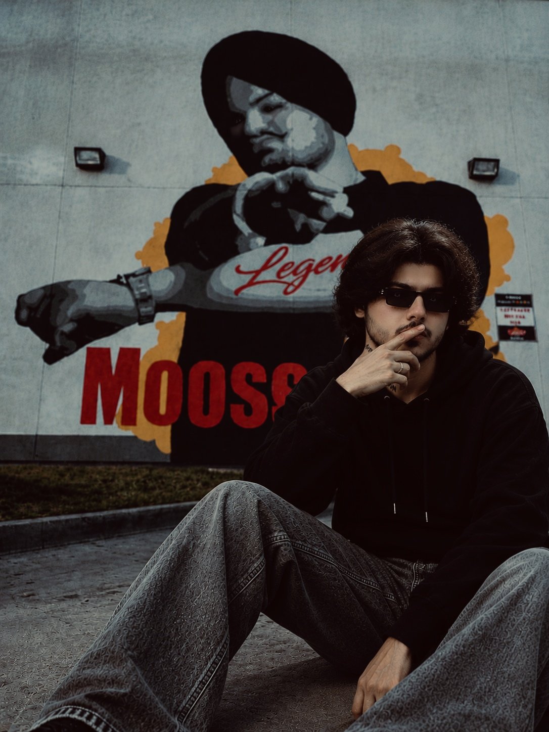 MEHAR-OG sitting in front of a Sidhu Moose Wala legend mural